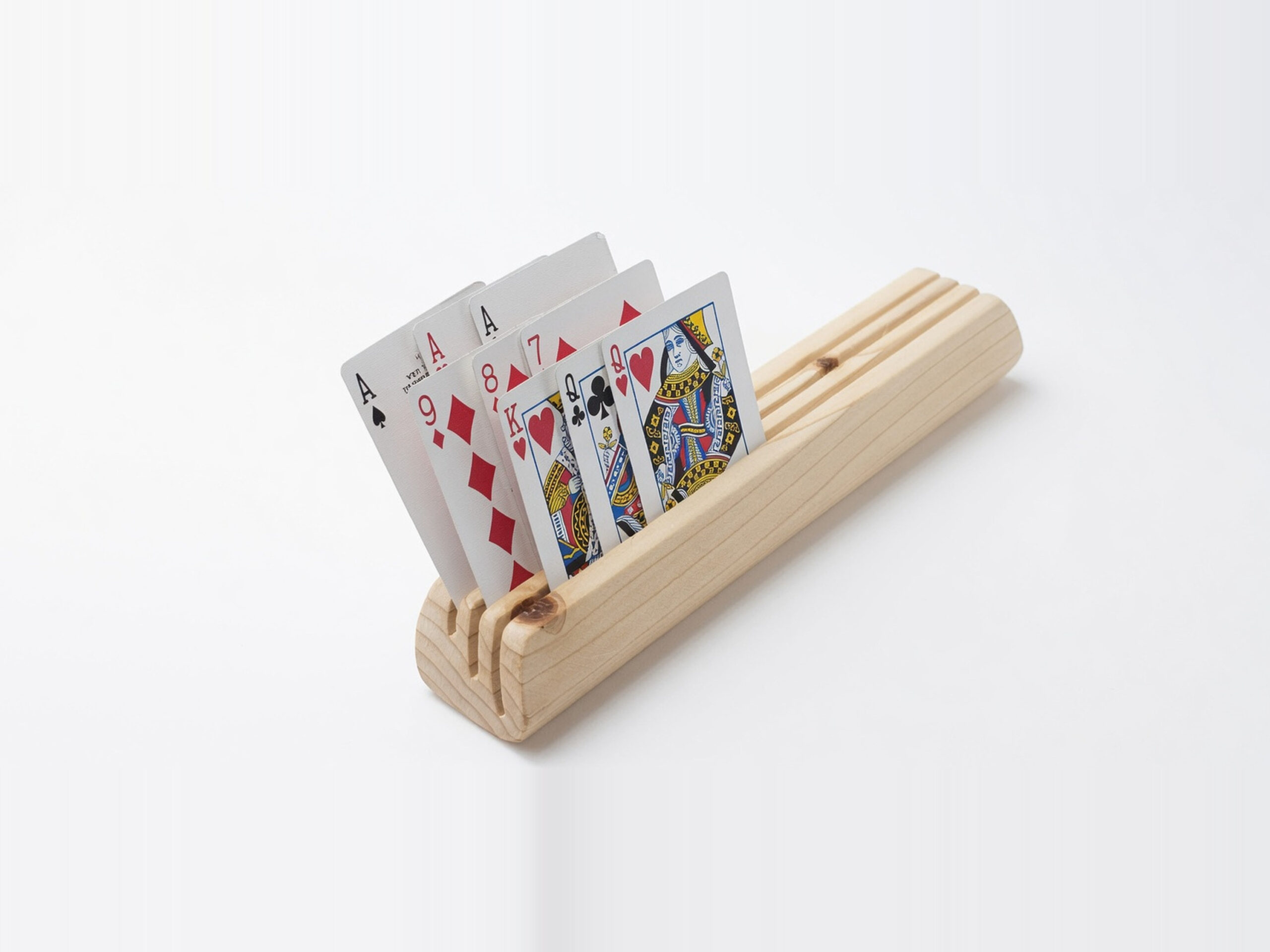 Angled view of a wooden playing card holder made from fir, holding face-up playing cards in three tiered angled slots on a white background.