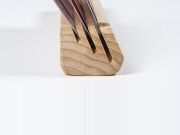 Close-up end view of a wooden playing card holder made from fir, with cards inserted into three angled slots of different depths, showing slot spacing and beveled profile.
