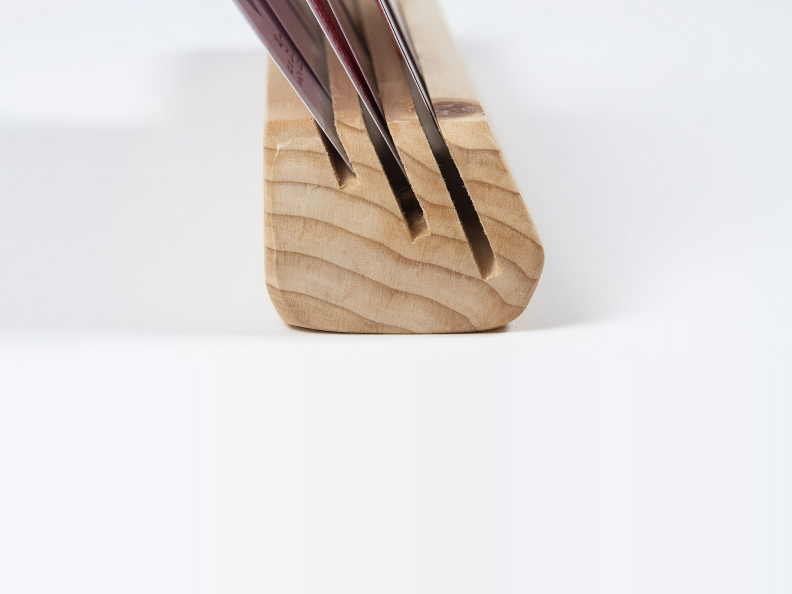 Close-up end view of a wooden playing card holder made from fir, with cards inserted into three angled slots of different depths, showing slot spacing and beveled profile.