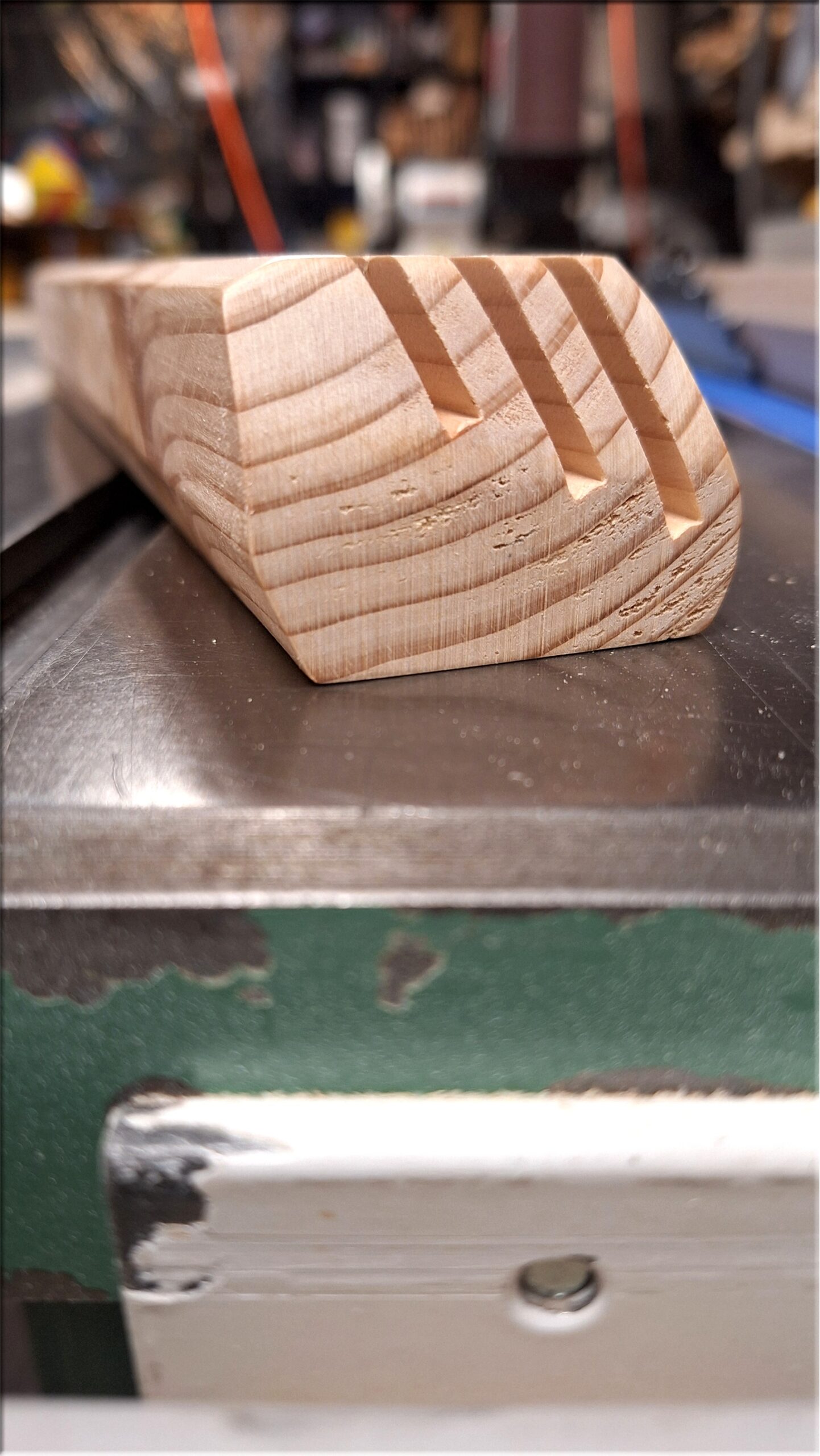 Close-up end profile of an unfinished wooden playing card holder made from fir in the workshop, showing three angled slots of different depths and the beveled profile.