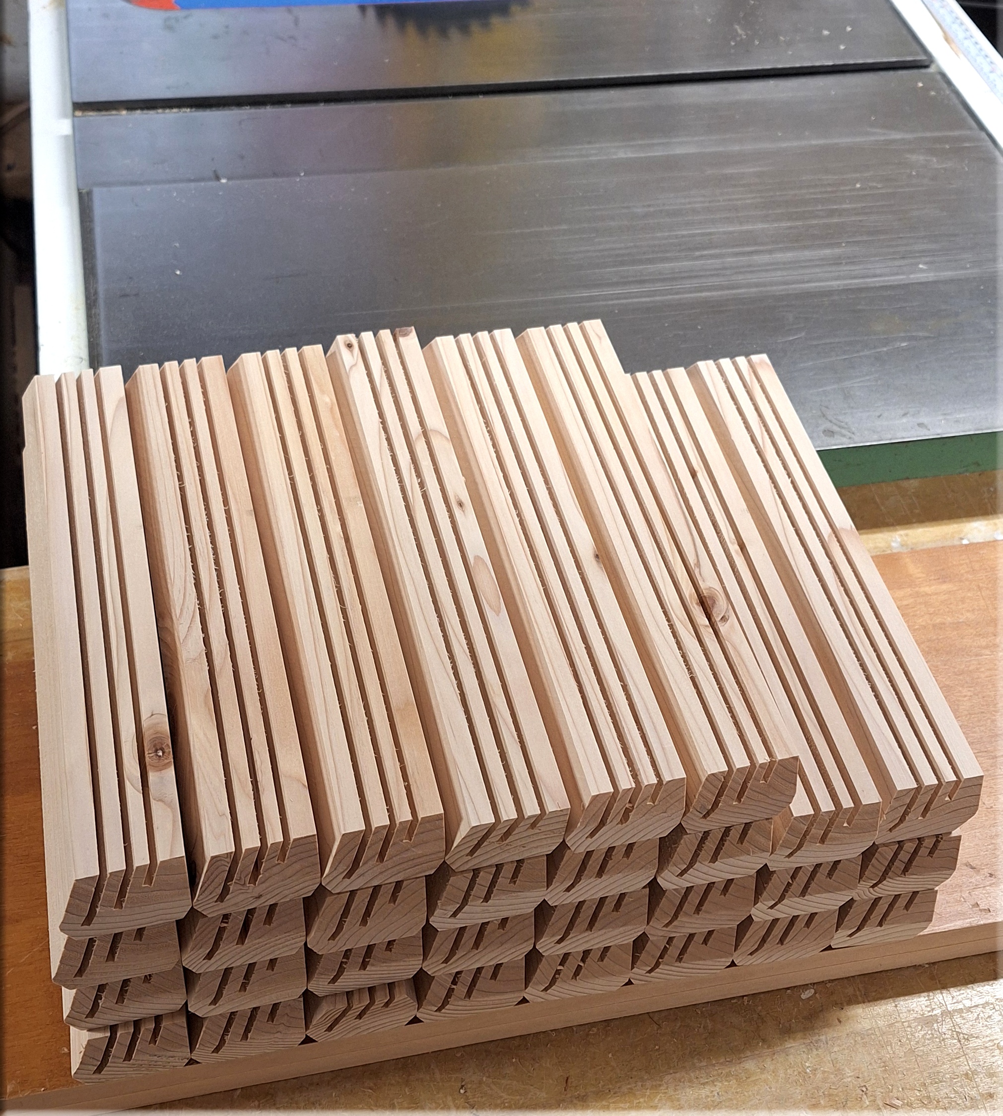 Stack of unfinished wooden playing card holders made from fir beside a table saw, showing three-slot construction, beveled profiles and natural wood grain.