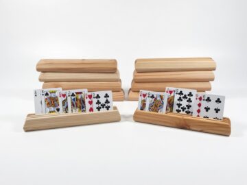 Ten wooden playing card holders made from fir on a white background, with two holding face-up cards and eight holders stacked behind them.