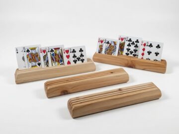 Four wooden playing card holders made from fir on a white background, with two holding face-up cards and two empty holders showing the three-slot design.
